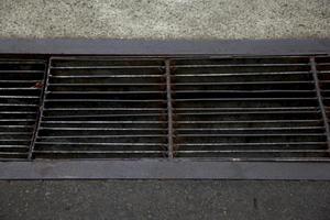 Sidewalk black metal waterway with rust and stains on concrete stone pavement. photo