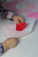 niño con carta con corazón de papel rojo, carta de amor para el día de san valentín, regalo para el día de la madre, niña pequeña que puso el corazón hecho a mano dentro del sobre, saludos navideños de la hija, maqueta para deseos de amor foto