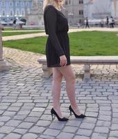 beautiful blonde model wearing a short black dress and high heels is having a photo shooting on the street