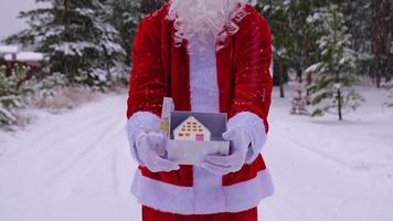 Santa Claus outdoor in winter and snow handing in hand gift box with house. Present for Christmas and New year, real estate, purchase, construction, relocation, mortgage, booking video