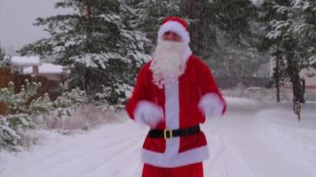 der weihnachtsmann hat spaß und lustiges tanzen, zeigt akrobatische tricks, kampfelemente und lustiges springen im winter im freien auf einer verschneiten straße mit kiefern. weihnachten und neujahr feiern. video