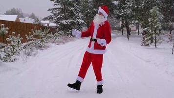 der weihnachtsmann hat spaß und lustiges tanzen, zeigt akrobatische tricks, kampfelemente und lustiges springen im winter im freien auf einer verschneiten straße mit kiefern. weihnachten und neujahr feiern. video