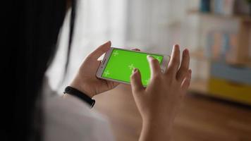 Closeup horizontal of hand woman using smartphone with green screen while lying on couch. Blank digital smartphone in hand girl. Showing content videos blogs tapping on center screen.