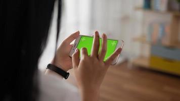 Closeup horizontal of hand woman using smartphone with green screen while lying on couch. Blank digital smartphone in hand girl. Showing content videos blogs tapping on center screen.