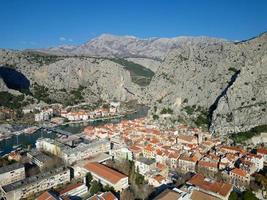 Aerial drone view of Omis town in Croatia. Location is where the Cetina River meets the Adriatic Sea.  Beautiful city next to the mountains and the sea. Travel and holidays destination. photo