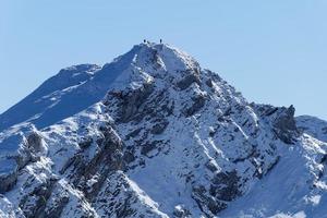 Hikers stand on the top of a mountain peak with snow. Hiking in the winter. Travel and free spirit feeling. photo