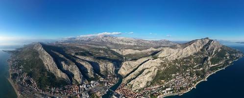 Aerial drone panorama view of Omis town in Croatia. Location is where the Cetina River meets the Adriatic Sea.  Beautiful city next to the mountains and the sea. Travel and holidays destination. photo