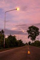 una vista de la luz de una farola naranja en una carretera mojada después de la lluvia con árboles en el campo tailandés. foto