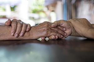 Low angle close-up shot of two wrinkled hands of two elderly Thai women holding each other in consolation. photo