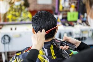 A close-up view of a man's back is a masked barber woman using a comb and clippers. photo