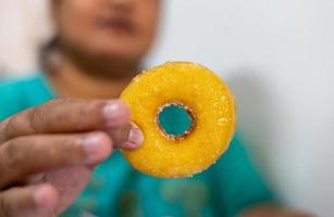 Low angle close up, fingers of a fat Thai woman holding a large yellow sugar-coated donut. photo