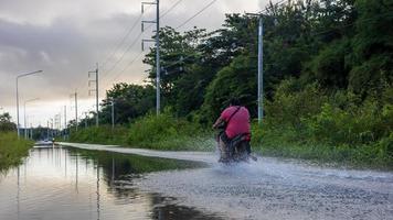 Behind the scenes, a fat man in a red shirt rides a motorbike on a flooded road. photo
