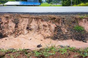 A side view of the sandstone soil beneath an asphalt road eroded by rain and wild water. photo
