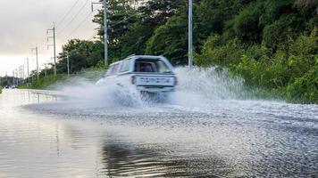 un coche blanco se está desdibujando en una carretera inundada que hace que el agua salpique. foto