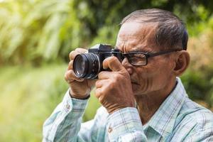 Close-up portrait of an elderly Thai man taking pictures with an old film camera. photo