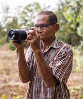 Portrait of an elderly Thai man wearing glasses holding an old DSLR camera. photo