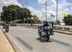 A couple riding motorcycles loaded with luggage to travel past a bridge with flags. photo