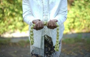 hermoso novio sosteniendo un collar de flores de jazmín y magnolia para una ceremonia de boda tradicional en indonesia foto