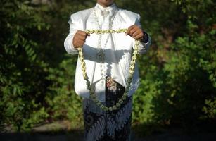 hermoso novio sosteniendo un collar de flores de jazmín y magnolia para una ceremonia de boda tradicional en indonesia foto