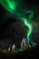 Green bright northern lights partially hidden by the clouds over Inuit living houses, Nuuk city, Greenland photo