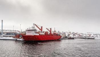 Big red cargo ship under the heavy snowfall in the port of Aasiaat, with village in the background, Greenland photo