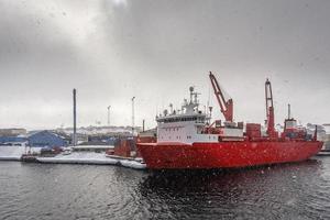 Big red cargo ship under the heavy snowfall in the port of Aasiaat, Greenland photo