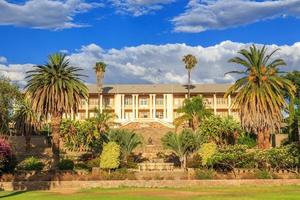 Park and garden with yellow palace building hidden behind tall palms, Windhoek, Namibia photo