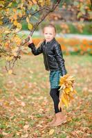 Adorable little girl with yellow leaves bouquet in fall on scooter photo