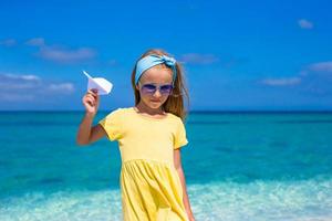 Happy little girl with paper airplane during beach vacation photo