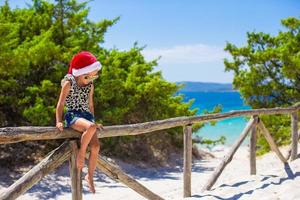 Adorable little girl in christmas hat during summer beach vacation photo