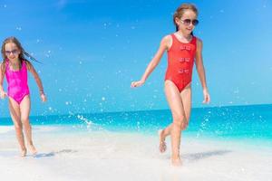 Little girls having fun at tropical beach playing together at shallow water photo