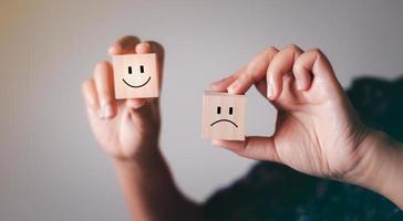 Hand showing mental health and emotional state concept, Smile face on bright side and sad face in dark side on wooden block cube for positive mindset selection. photo