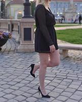 beautiful blonde model wearing a short black dress and high heels is having a photo shooting on the street