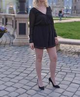 beautiful blonde model wearing a short black dress and high heels is having a photo shooting on the street