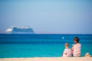 Young mom and adorable girl at beach on sunny day with view of big liner photo