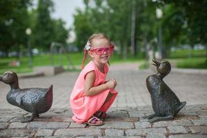 Cute girl sits next a duck figure of iron and having fun photo