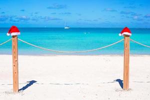 Two Santa hats on fence at tropical white beach photo