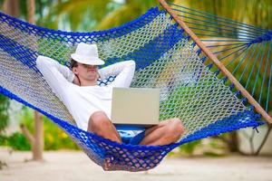 joven con laptop en hamaca en vacaciones tropicales foto