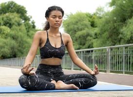 African American woman practicing yoga outdoor in a tranquil nature park. Female person leisure activity is meditation, relaxation mindfulness exercise for healthy lifestyle and peaceful spirituality. photo