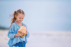niña adorable con coco grande en la playa de arena blanca foto