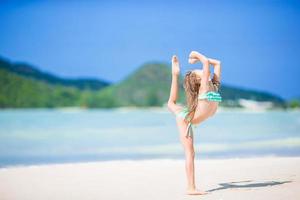 Beautiful little girl doing sporty exercises on the beach photo