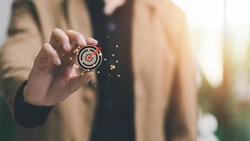 Wooden block in businessman hand and arrow icon hitting center of dartboard target,Setting business goals and focused concepts, Organizational growth and objectives, marketing strategy planning photo