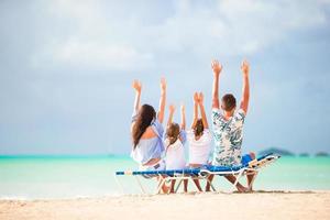 Happy beautiful family on the beach. Back view of parents and kids on the chaise-lounge photo