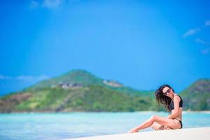 Woman sitting on beach laughing and enjoying summer holidays looking at the camera. Beautiful model in bikini sitting down. photo