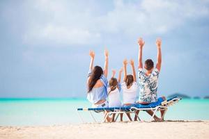 Happy beautiful family on the beach. Back view of parents and kids at sunbed photo