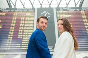 pareja joven en el aeropuerto internacional mirando el tablero de información de vuelo foto