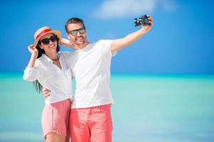 Happy couple taking a selfie photo on white beach. Two adults enjoying their vacation on tropical exotic beach