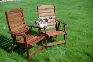 dos sillas de madera sobre la hierba con un jarrón de flores sobre ellas foto