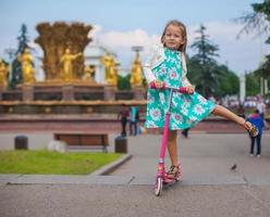 Cheerful cute toddler girl on the scooter in a park photo