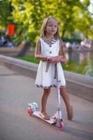 Beautiful toddler girlin dress on the scooter in a park photo